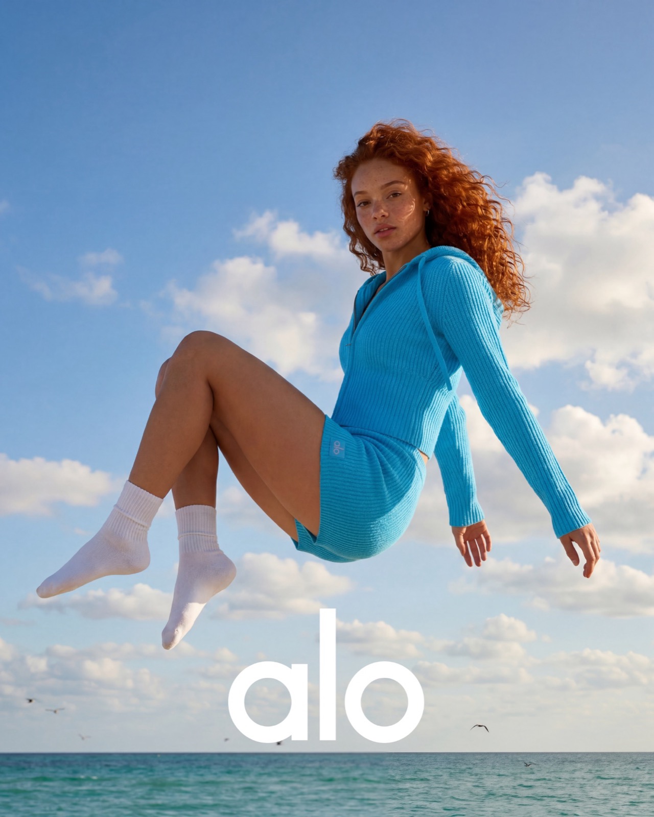 A figure suspended against sky and sea in ribbed cobalt knit