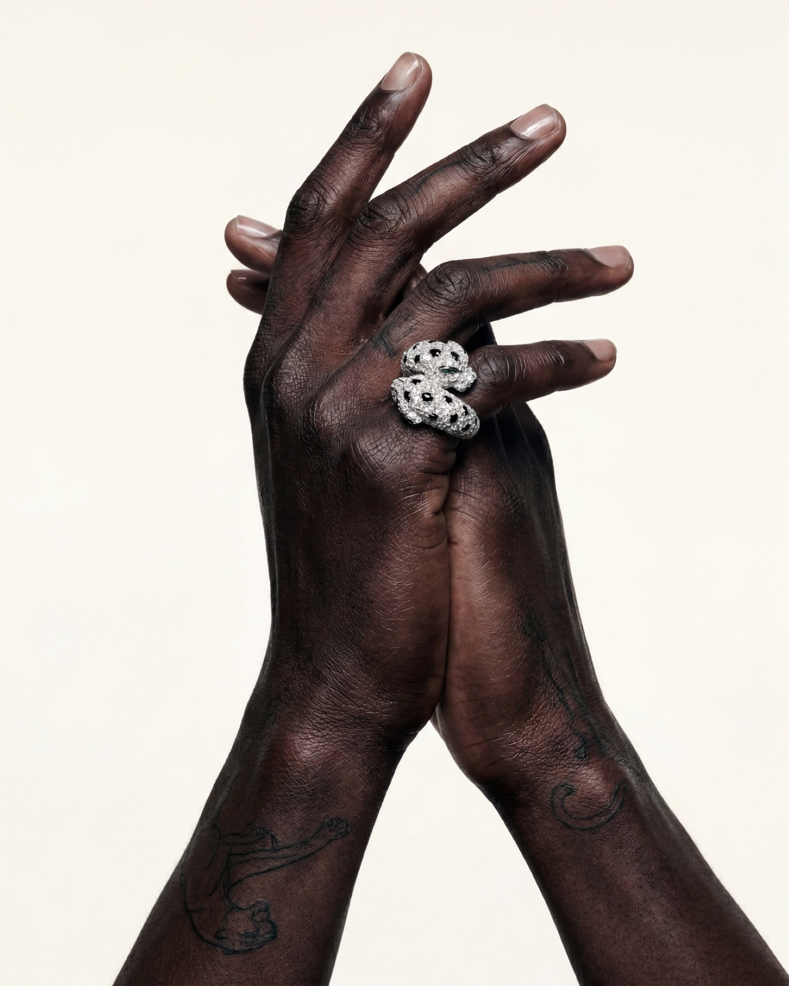 Two hands crossed at the wrist, a panther tattooed on the skin beneath the panther ring