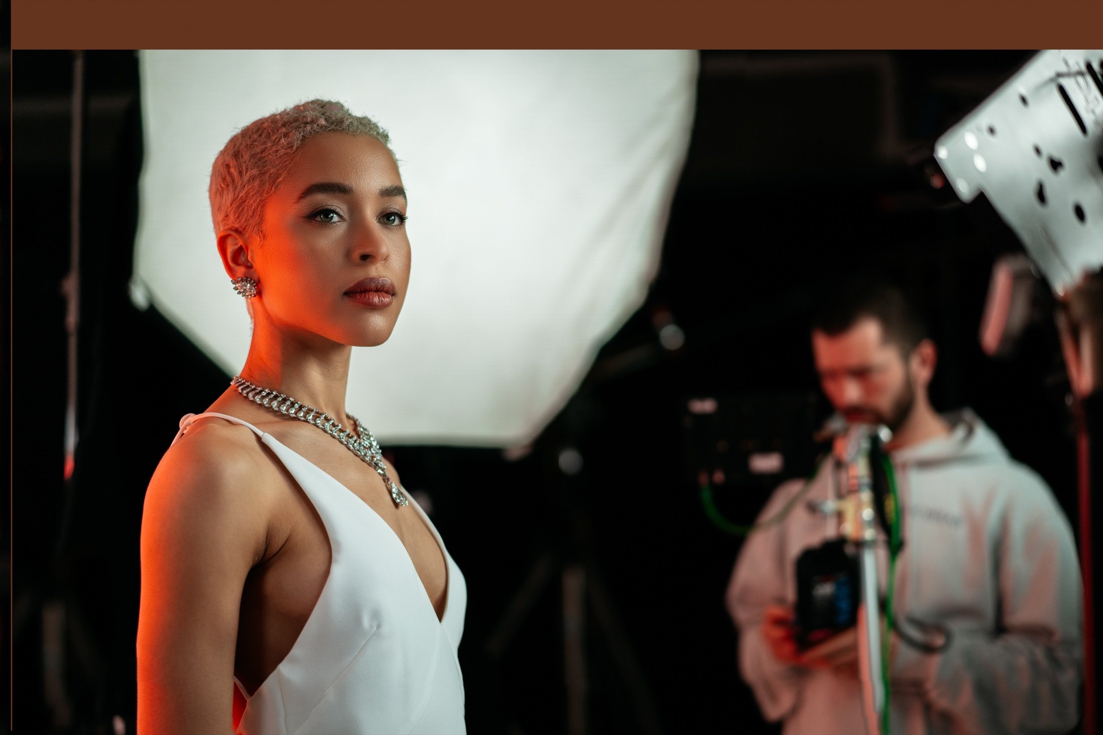 Model on set under warm light with crew behind